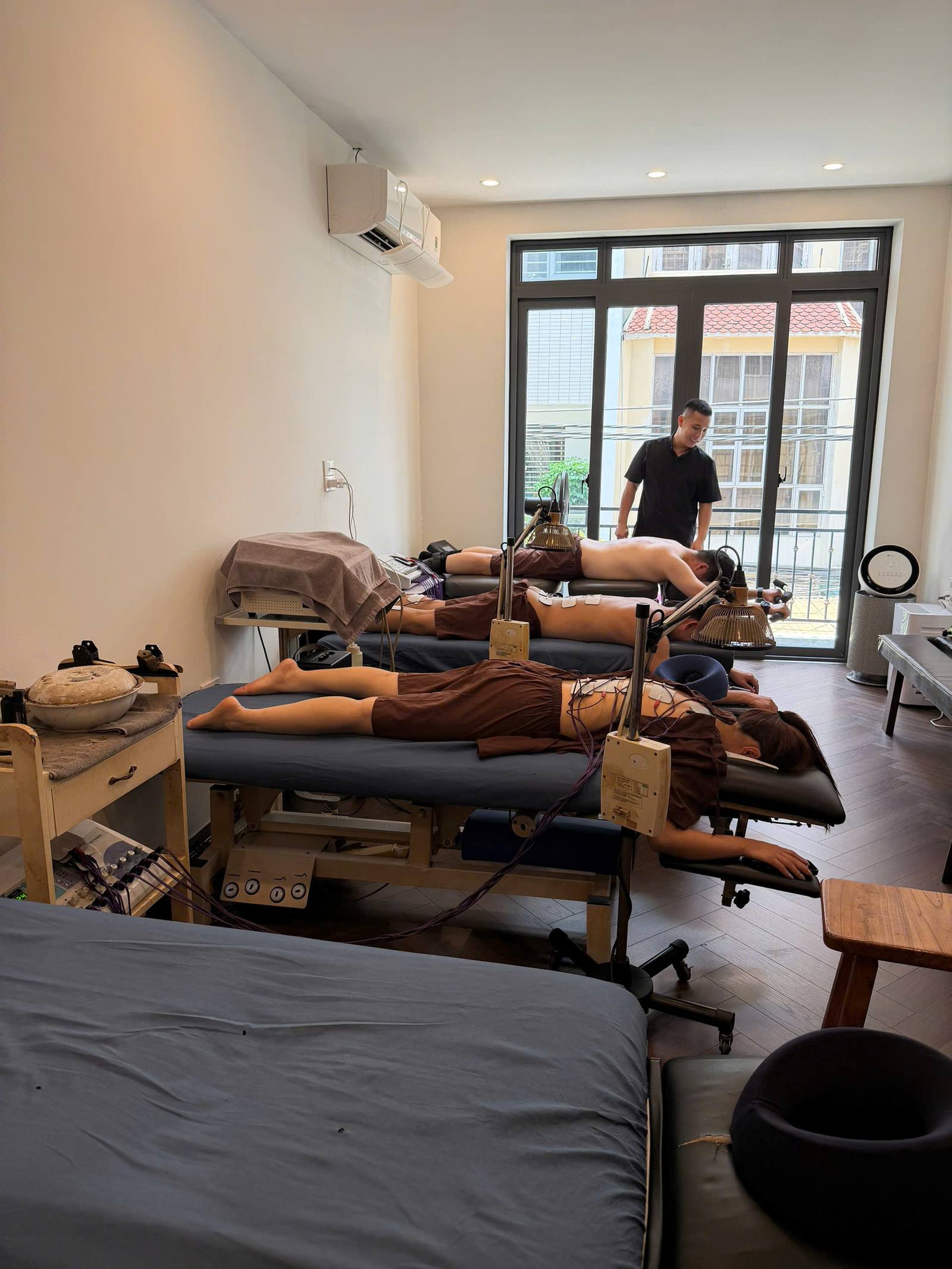 Phòng trị liệu tại 24 ngõ 523 Minh Khai — ba bàn trị liệu, máy điện xung và đèn hồng ngoại đang hoạt động